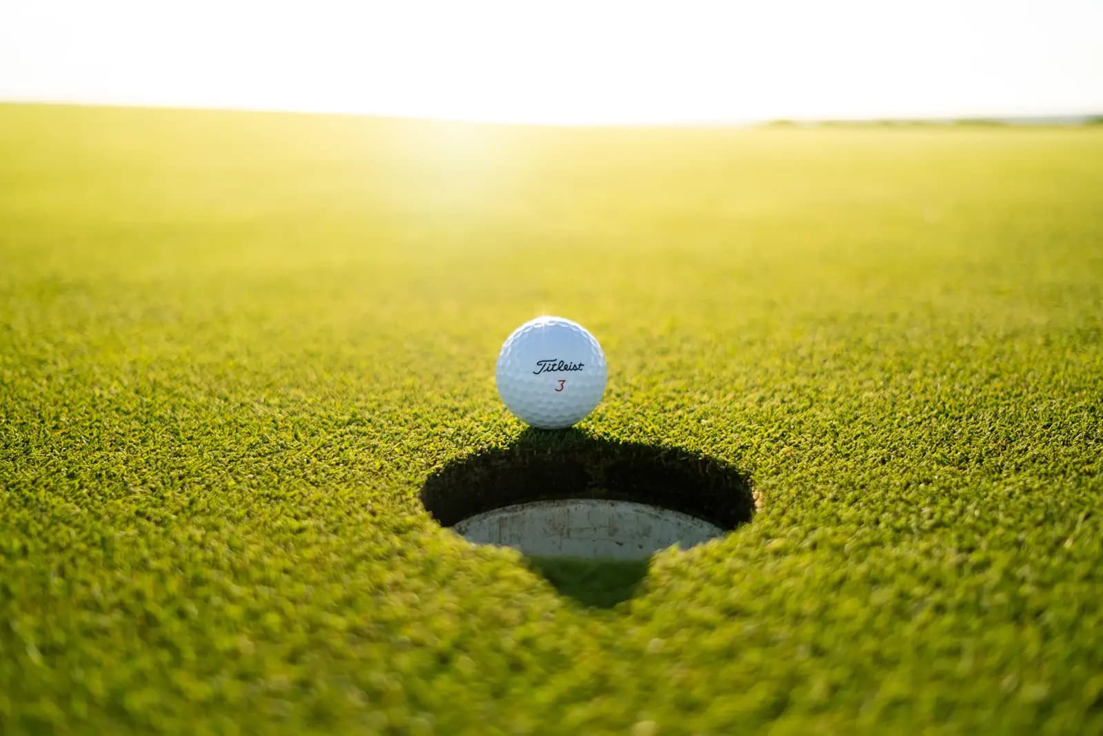 Bola de golf al borde del hoyo con la luz del atardecer