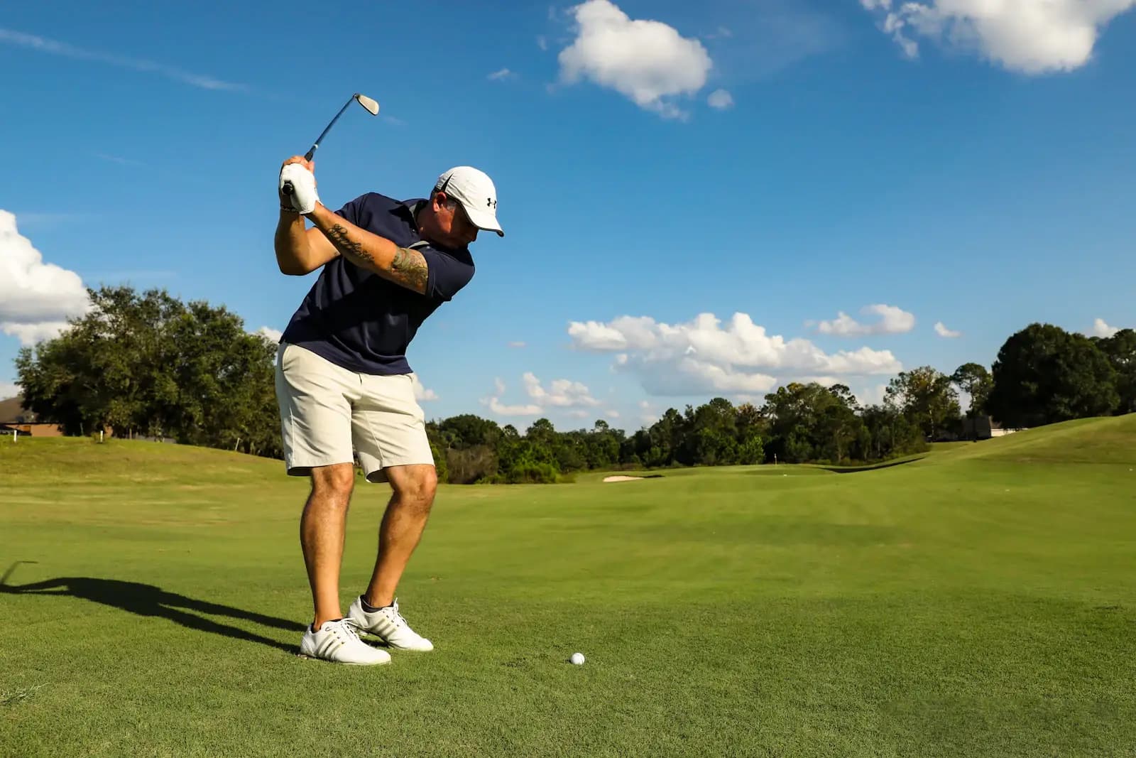 Golfista terminando el swing en un fairway soleado bajo cielo azul